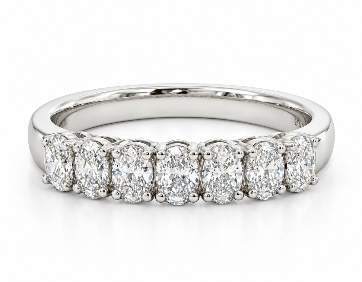 A white gold diamond band ring featuring seven oval-cut diamonds in a row, set in a polished silver-colored metal band.
