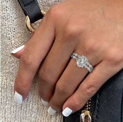 A hand with white manicured nails wears the Romance Semi-Mount Diamond Engagement Ring, holding a black purse.
