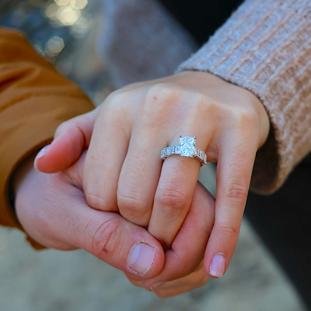 Man holding a woman's hand, displaying a white gold ring with prominent diamond jewel
