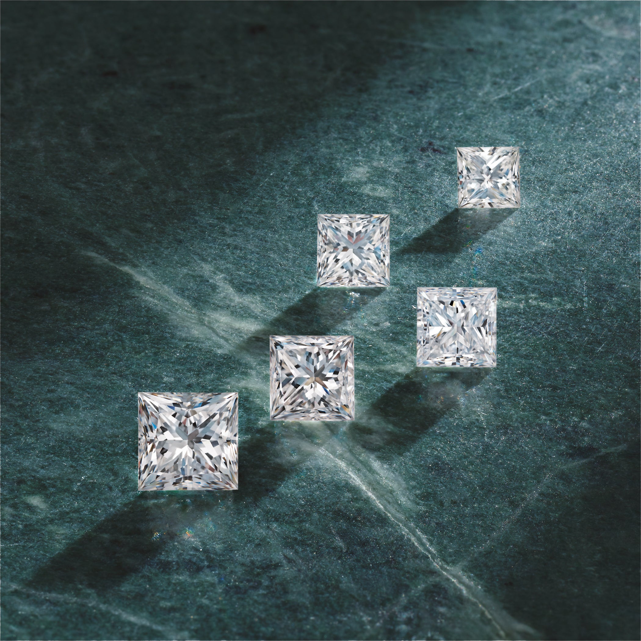 Five square-cut diamonds on a green marble surface