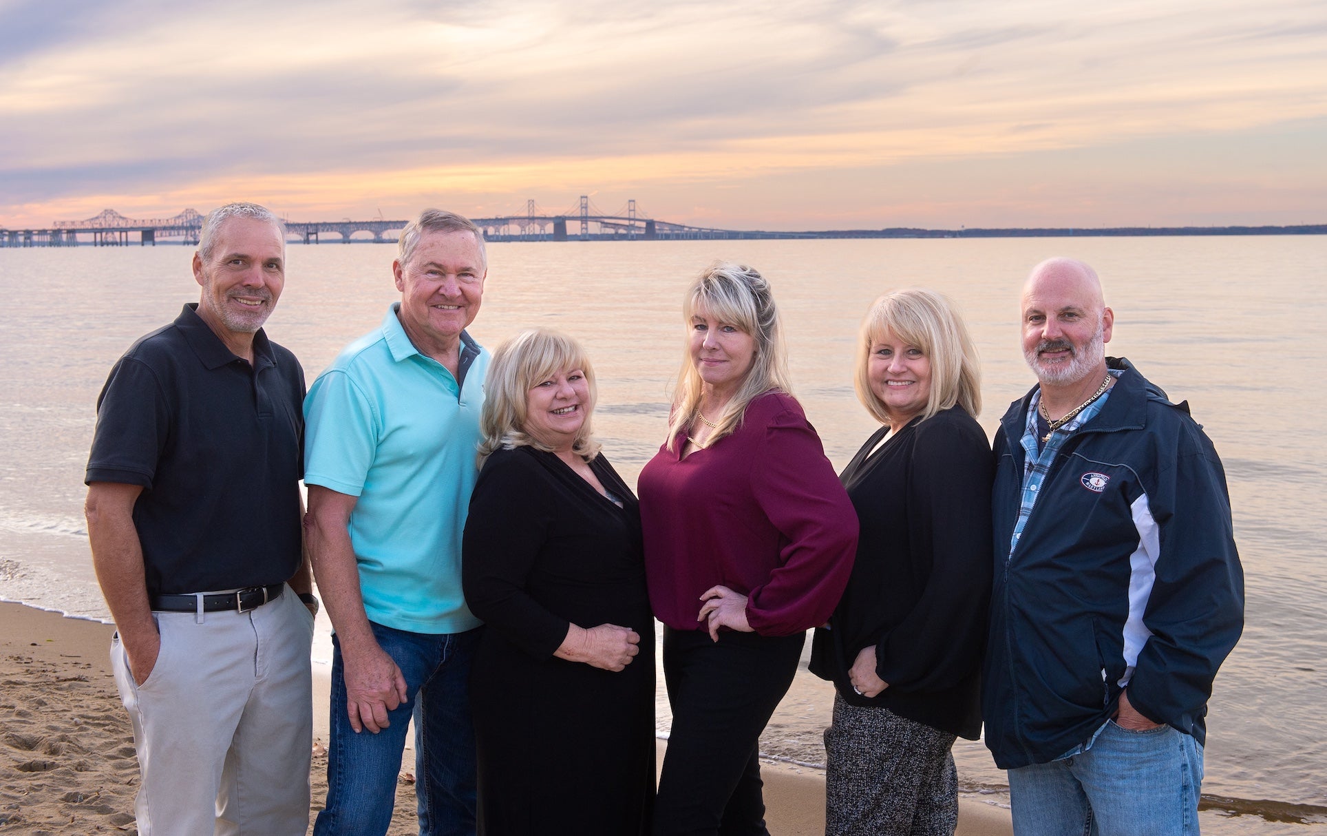 Group of 6 Kent Island Jewelry Employees posing on the shores of the Chesapeake with the Bay Bridge behind them