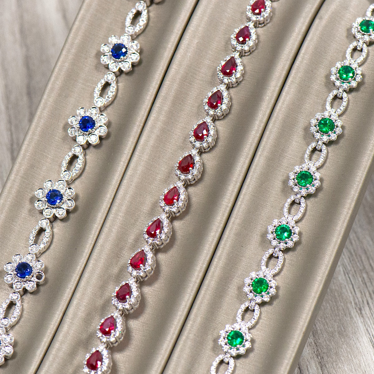Three jeweled bracelets, one sapphire, one ruby, and one emerald, draped over a beige display