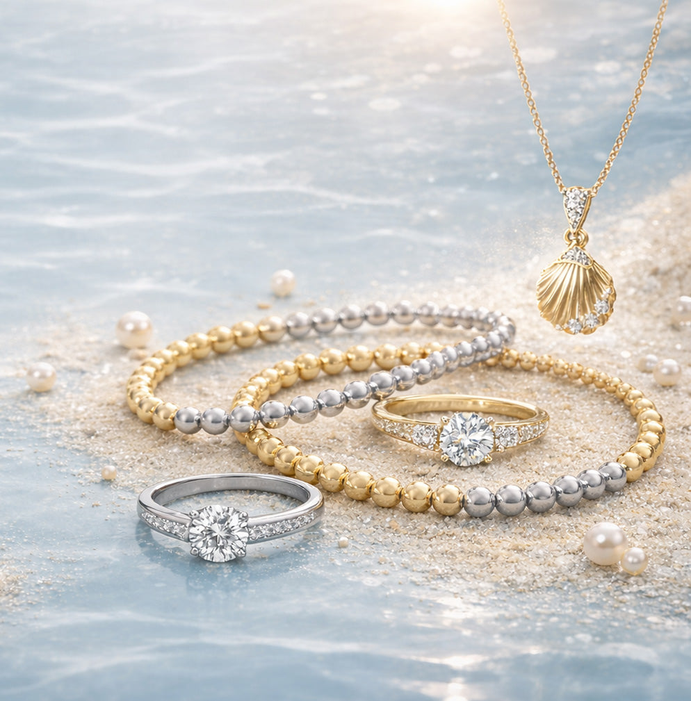 A set of jewelry, including rings, bracelets, and a necklace with a shell pendant, sitting on a sandy background