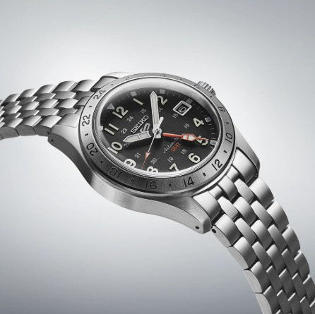 The Seiko 5 Sports SS Automatic GMT Black Dial Watch by Seiko features a date display and silver link band on grey.