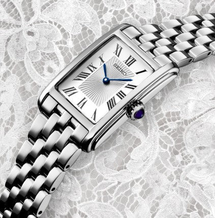 Seiko Essentials SS Quartz White Dial Watch with blue hands and Roman numerals on a stainless steel bracelet.