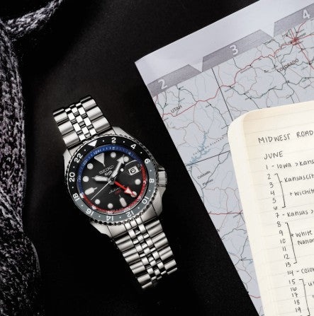 A Seiko 5 Sports SS Automatic GMT Charcoal Dial Watch by Seiko rests next to a map and notebook with Midwest trip plans.
