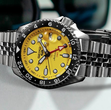 The Seiko 5 Sports SS Automatic GMT features a yellow dial, black bezel, and stainless steel bracelet in close-up.