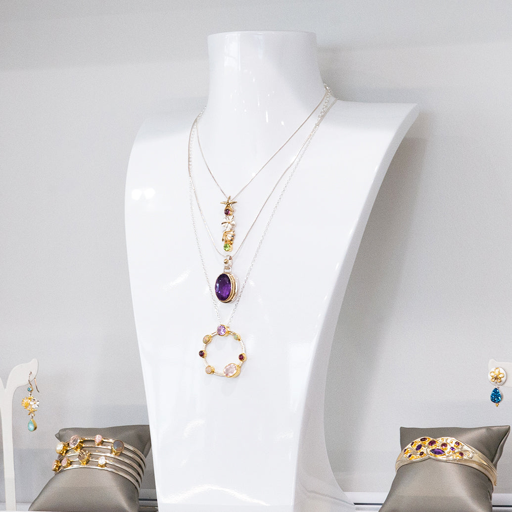 Jewelry set including a necklace, earrings, and bracelets on a mannequin and gray stands against a white background.