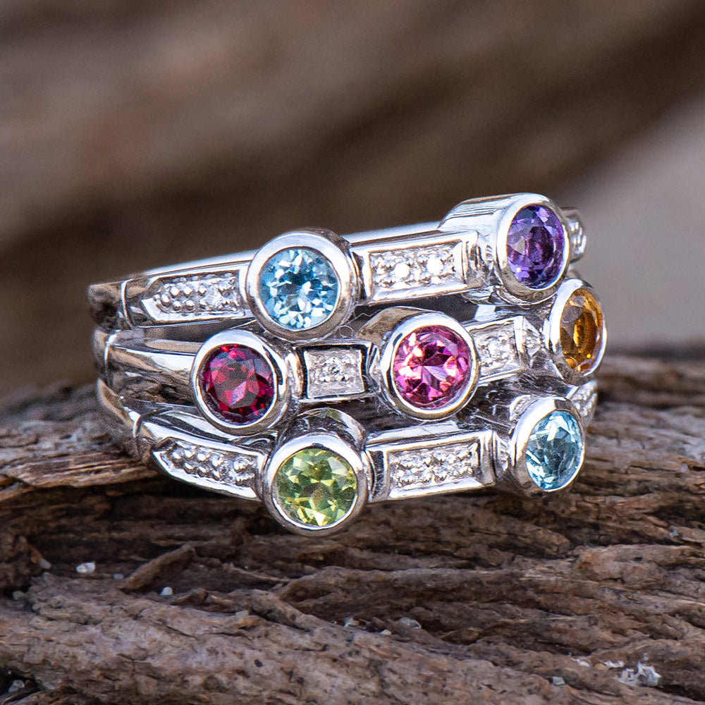Stack of silver rings with multicolored gemstones on a wooden surface