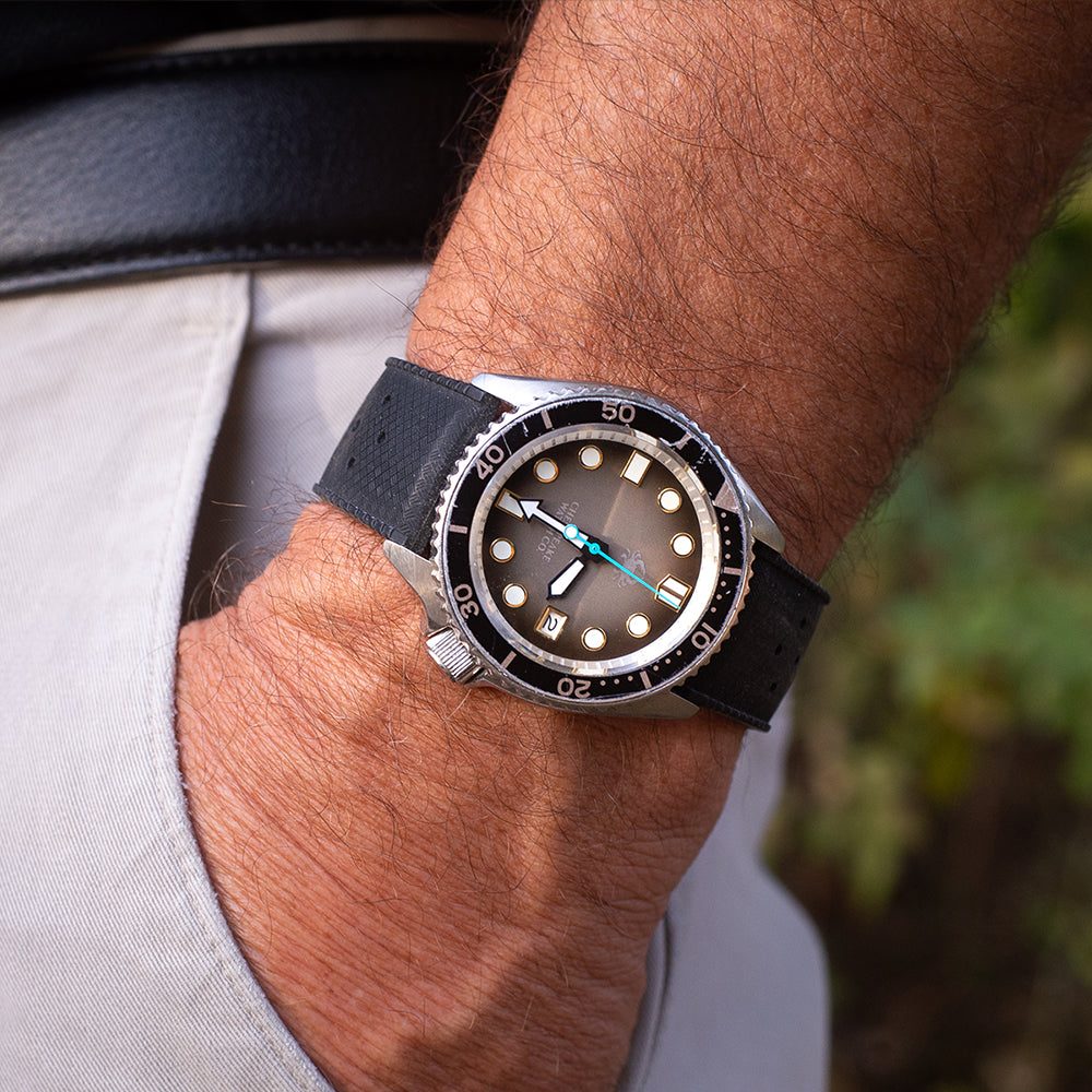 Close-up of a wrist wearing a black wristwatch with a detailed face.