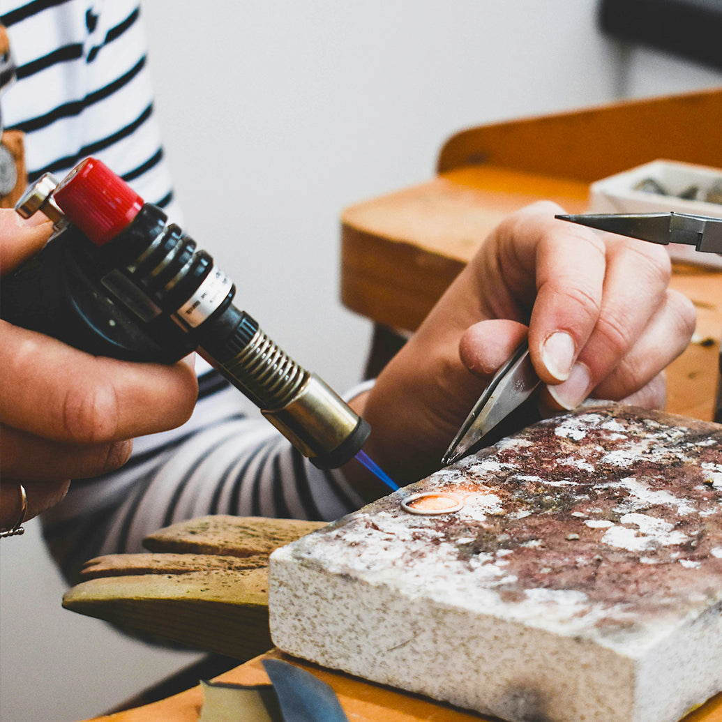Jeweler using a torch to heat and manipulate a ring