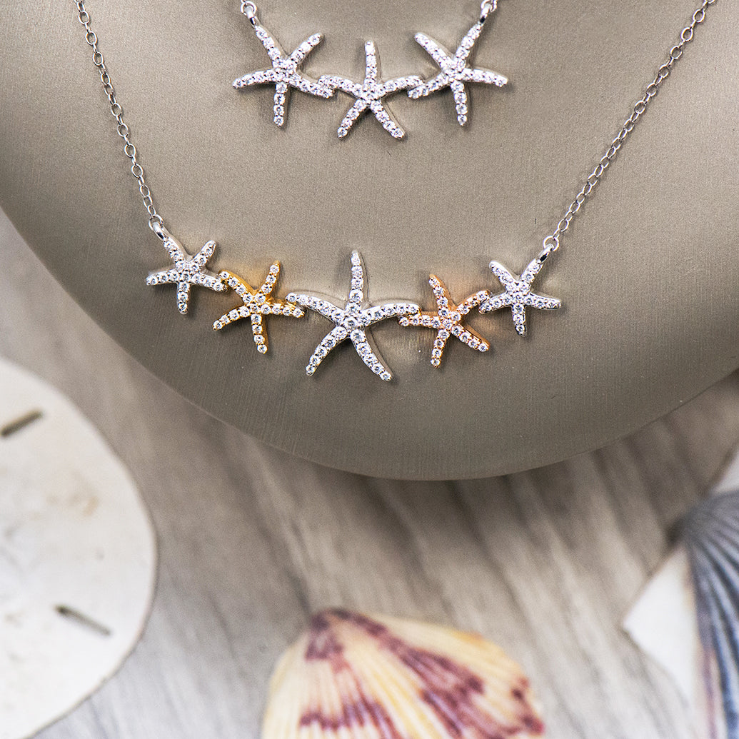 Two necklaces with diamond starfish pendants draped over a display bust with shells in the foreground
