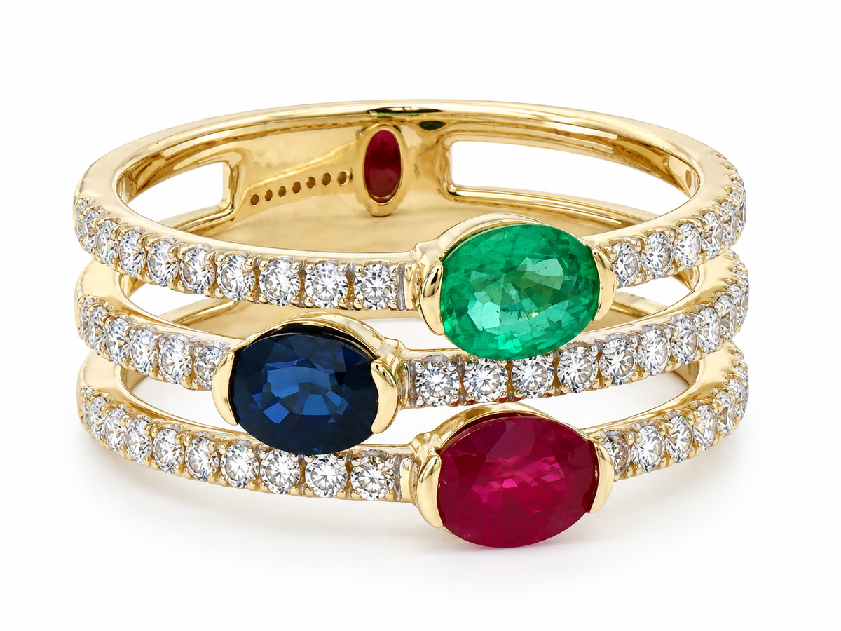A gold triple-band ring featuring oval-cut emerald-cut green, blue, and pink gemstones, accented with pavé-set round diamonds on a clean white background.