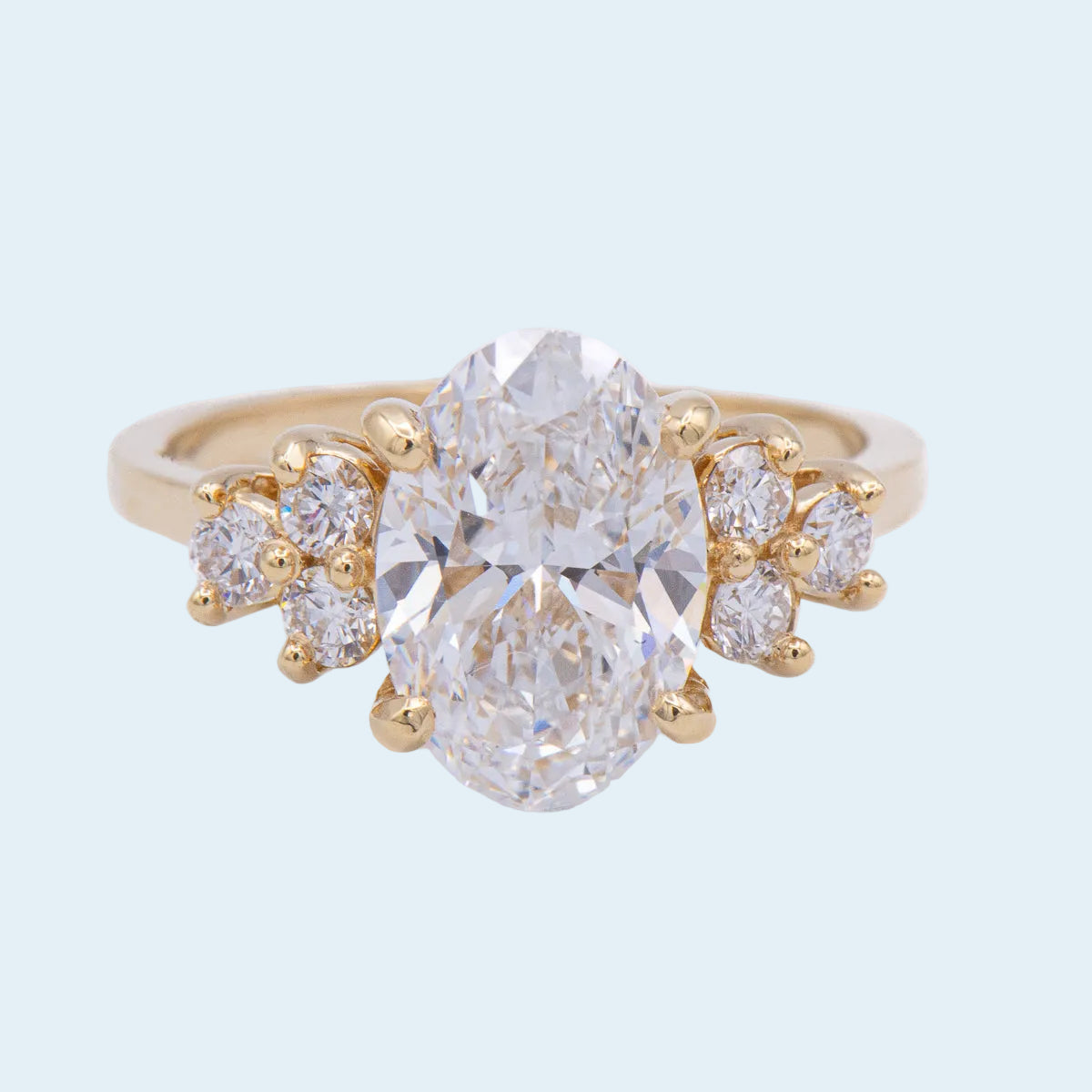 Gold ring with a large central diamond and smaller diamonds on a light blue background