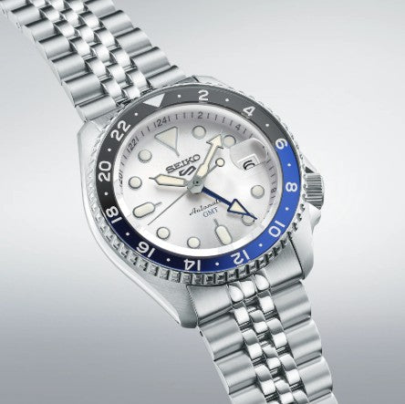 Seiko Automatic 5 Sports SKX GMT watch with blue-black bezel, white dial, and metal bracelet on light background.