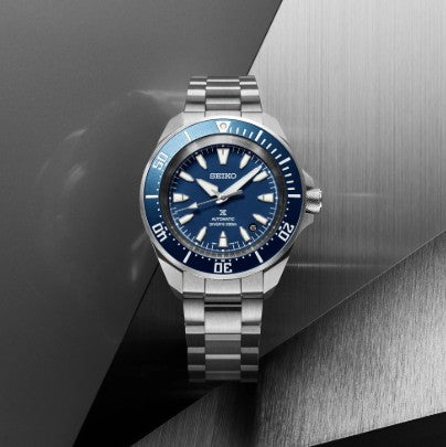 The Seiko Prospex Diver SS Automatic Blue Dial Watch is displayed on brushed metal and matte gray backgrounds.