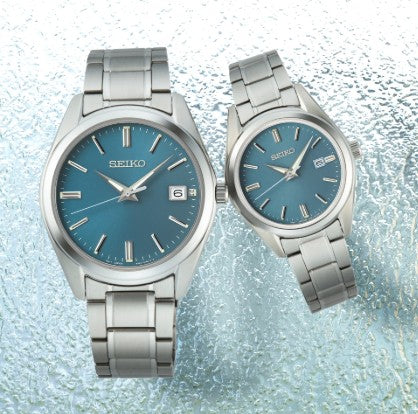 Two Seiko Essentials SS Quartz Blue Dial Watches with sapphire crystal on a textured background.