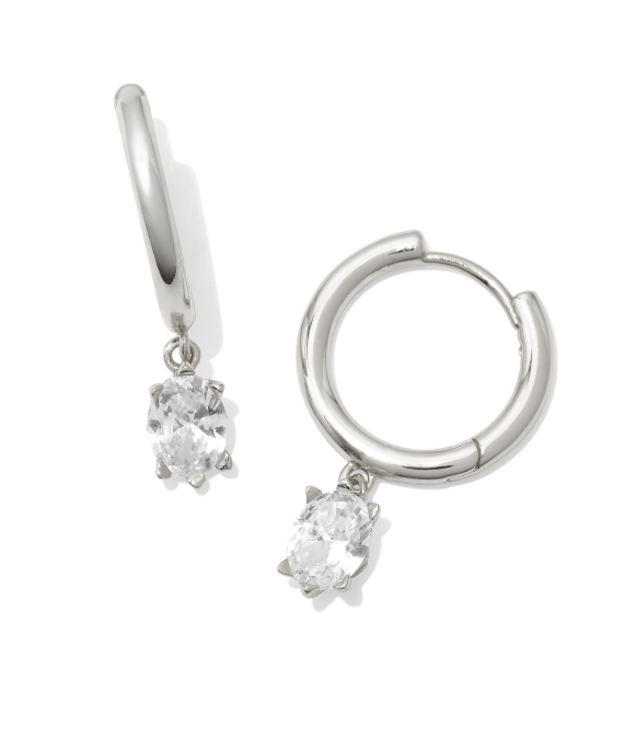 Kendra Scott CAILIN silver huggie earrings, each with an oval-cut white crystal in a claw setting.