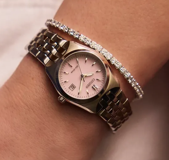 A close-up of a wrist wearing a Citeo watch with a pink dial and silver-tone metal bracelet, alongside a thin diamond-studded bracelet.
