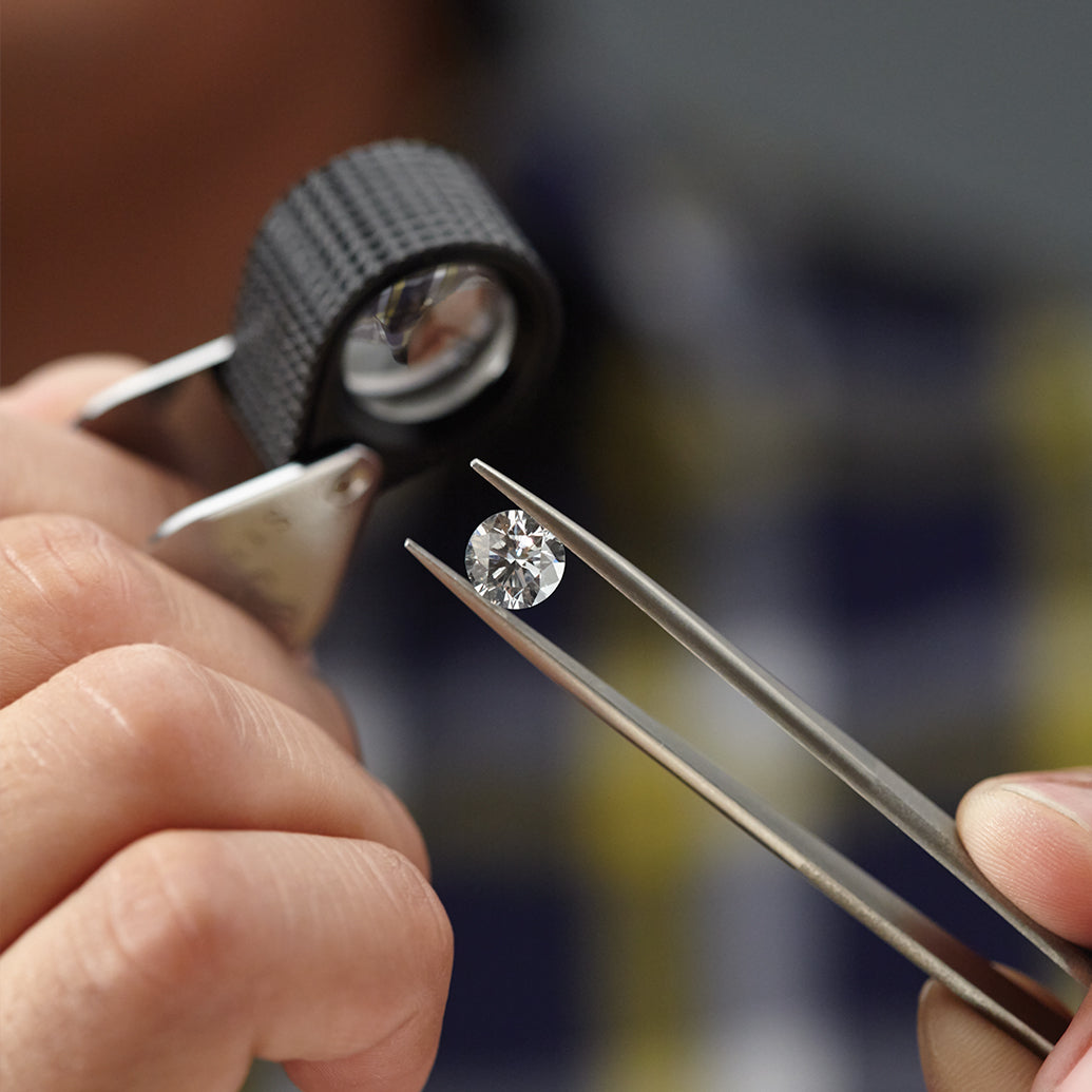 Person holding a diamond between tweezers with a magnifying glass in the background