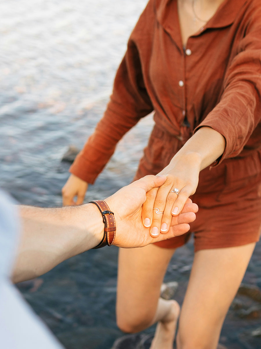 A recently engaged couple holding hands by a body of water.