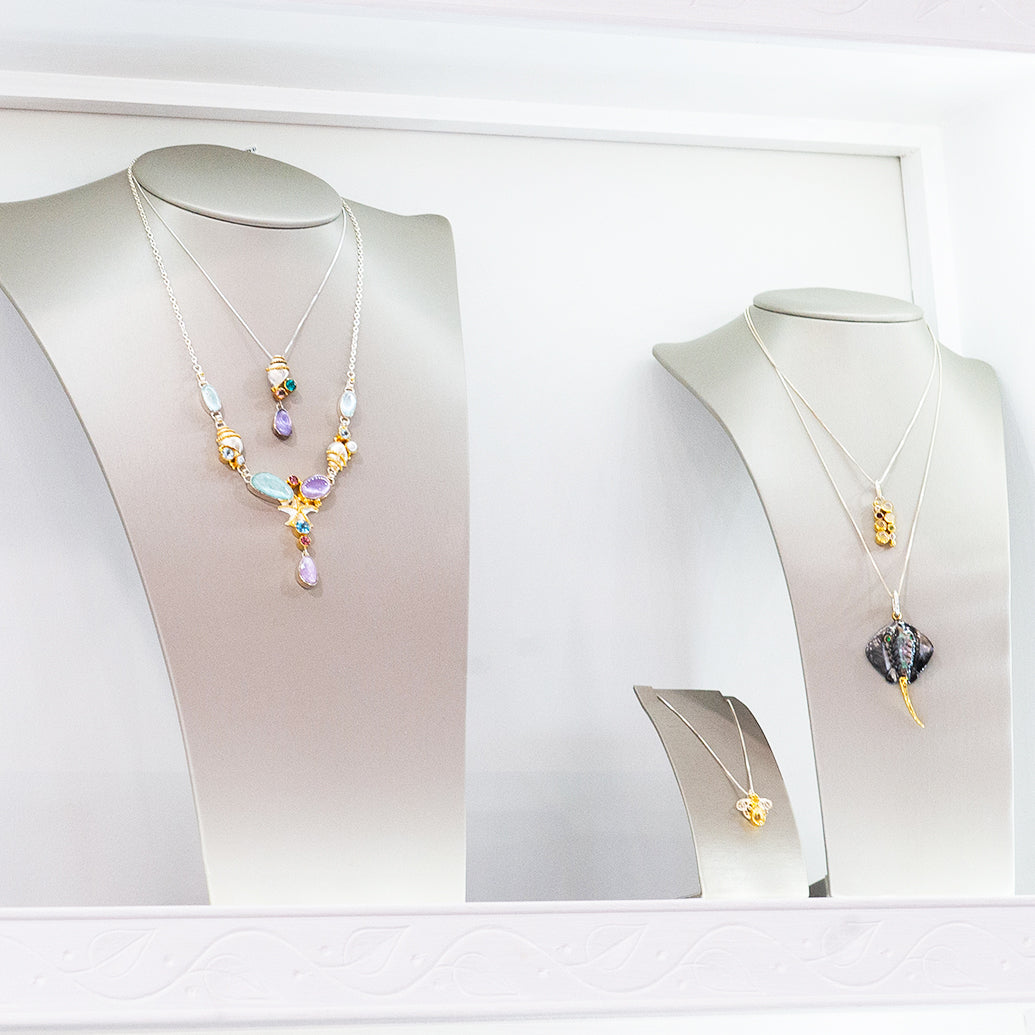 A colorful gemstone pendant necklace and a custom stingray shaped pendant necklace displayed on white mannequin busts