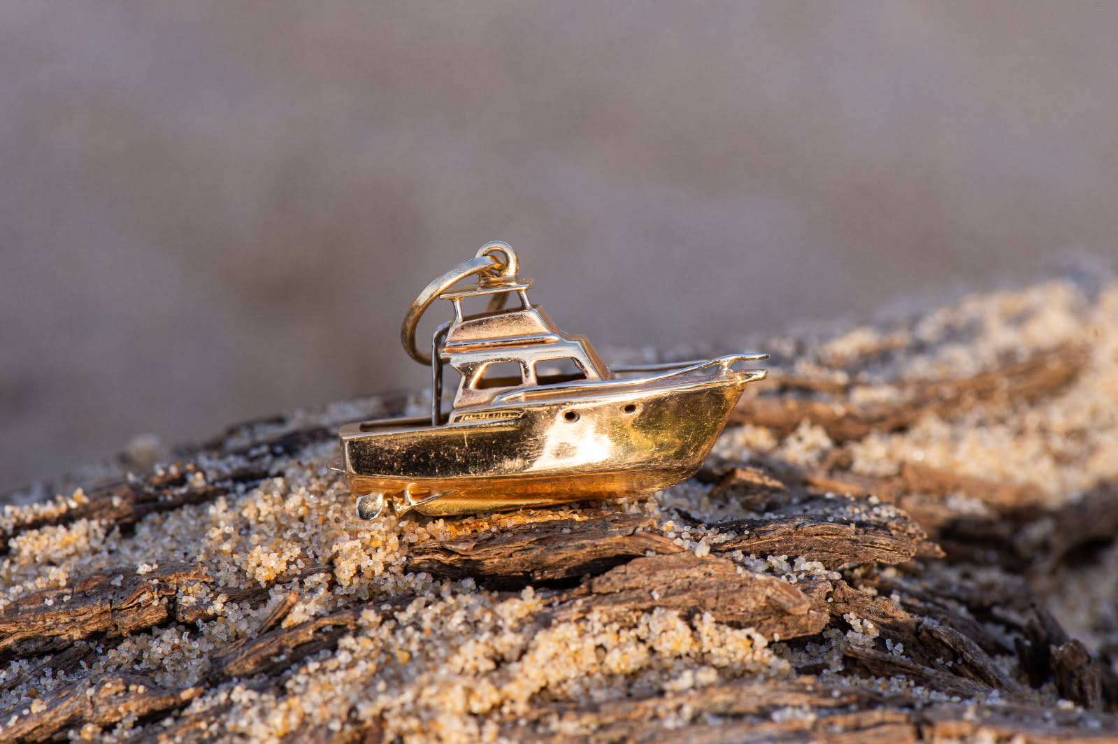 Gold boat pendant sitting on a sandy, wooden surface.