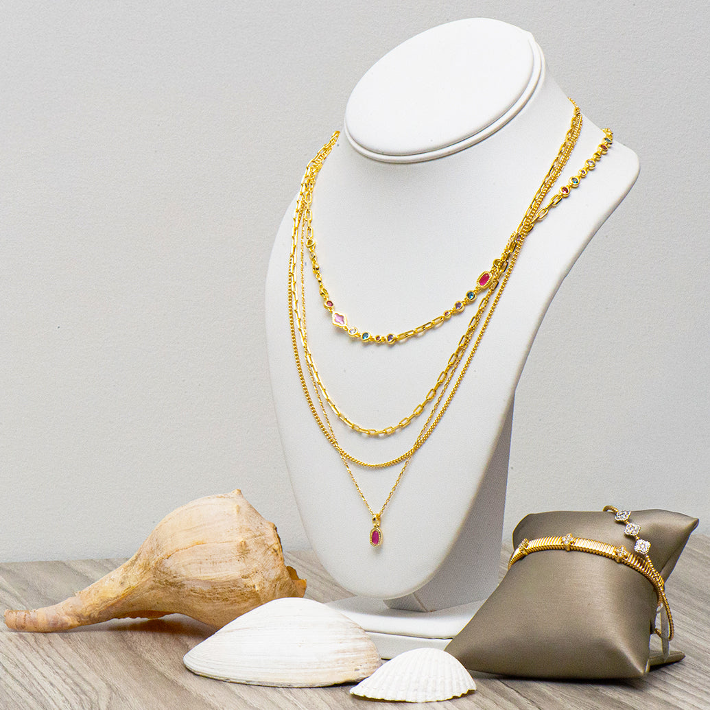Gold necklaces on a mannequin bust with seashells and a bracelet pillow on a wooden surface