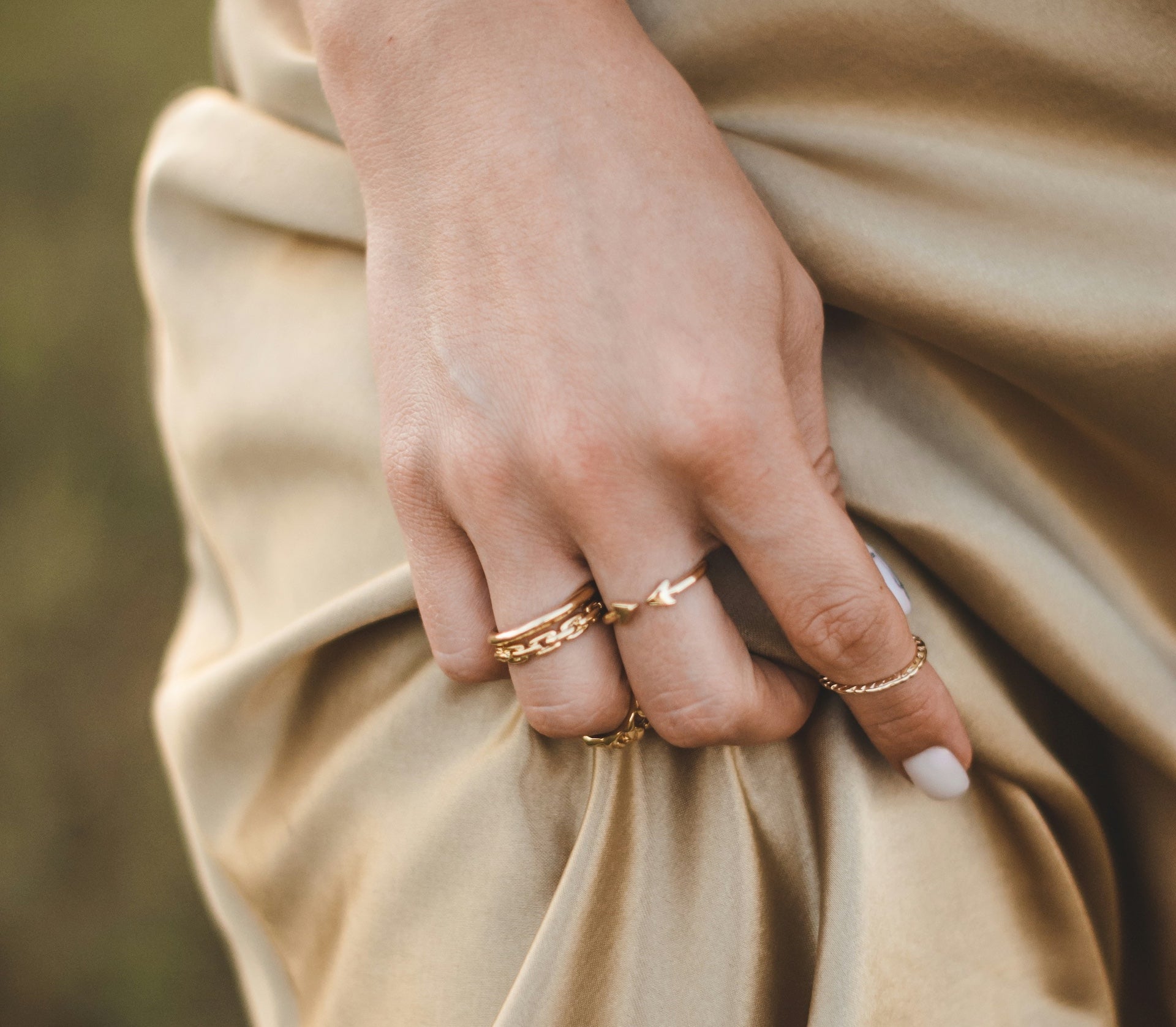 Hand wearing multiple gold rings on a beige fabric background