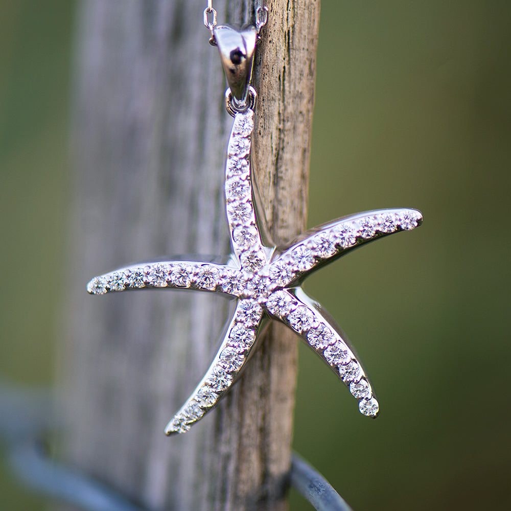 Starfish-shaped pendant with clear stones on a wooden post against a blurred green background