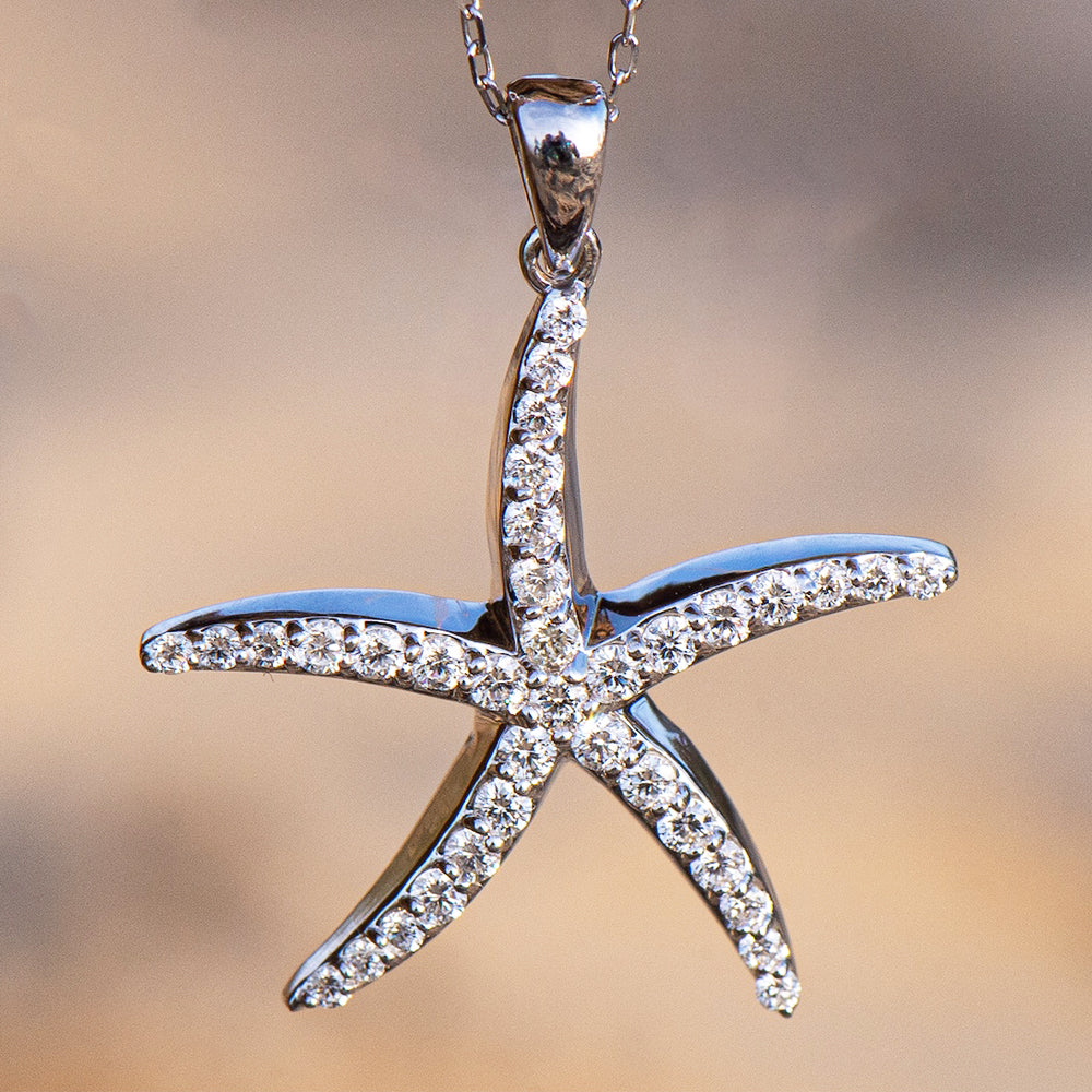 Silver starfish pendant with diamond accents, displayed on a blurred background.